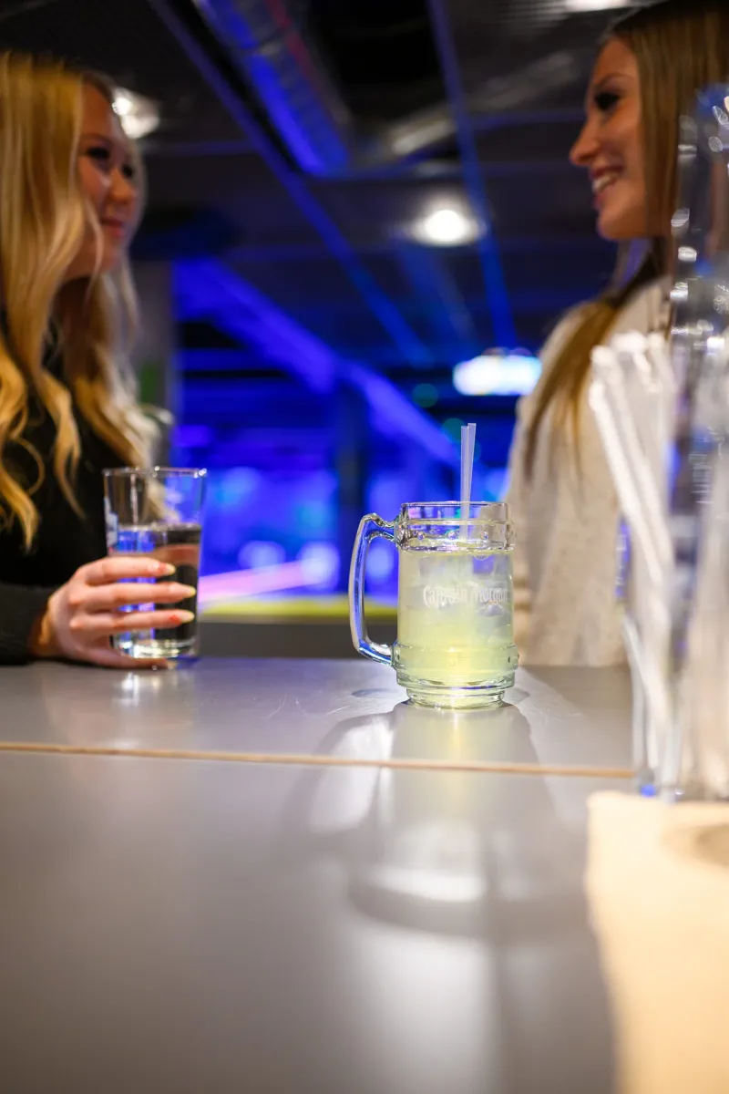 Kaksi asiakasta istuu baaritiskillä, UV-valot taustalla
